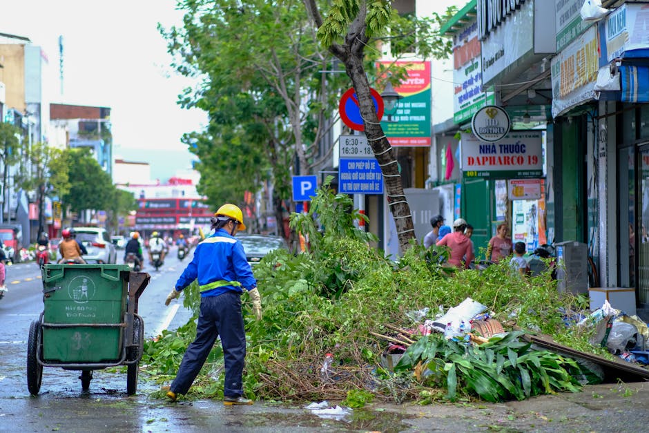A city worker clears green waste on a street in Da Nang, Vietnam, showcasing urban maintenance efforts.